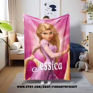 May include: A pink fleece blanket featuring a cartoon illustration of a princess in a purple dress with long blonde hair. The princess's name, "Jessica", is written in white script. The blanket is held up in front of a person.