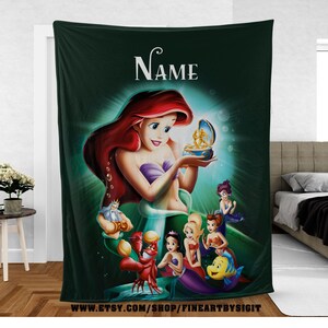 May include: A dark green throw blanket featuring a colorful illustration of Ariel from The Little Mermaid. The image includes Ariel, King Triton, Sebastian, Flounder, and other characters. The word "Name" is at the top.