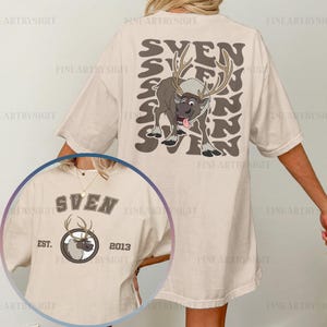 May include: Beige t-shirt featuring a cartoon image of Sven the reindeer with the word "SVEN" repeated in a stacked design. The front of the shirt has a smaller Sven graphic with the text "SVEN EST. 2013".