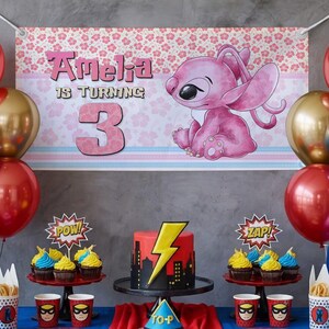 May include: A birthday party scene with a banner that reads "Amelia is turning 3." The banner features a pink cartoon character and floral patterns. The table has a cake with a lightning bolt design, cupcakes, and superhero-themed cups and decorations.