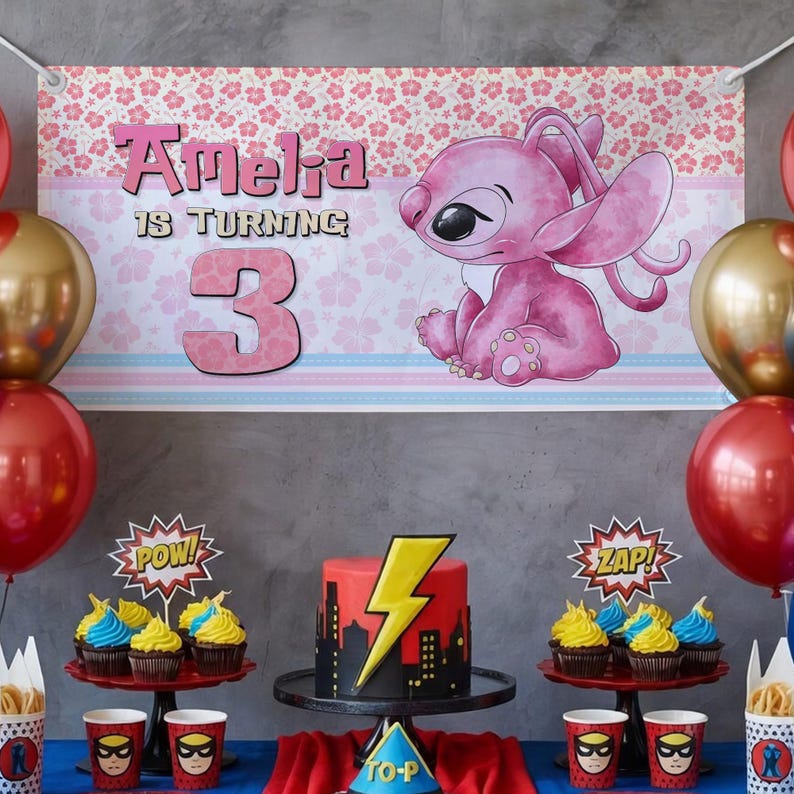 May include: A birthday party scene with a banner that reads "Amelia is turning 3." The banner features a pink cartoon character and floral patterns. The table has a cake with a lightning bolt design, cupcakes, and superhero-themed cups and decorations.