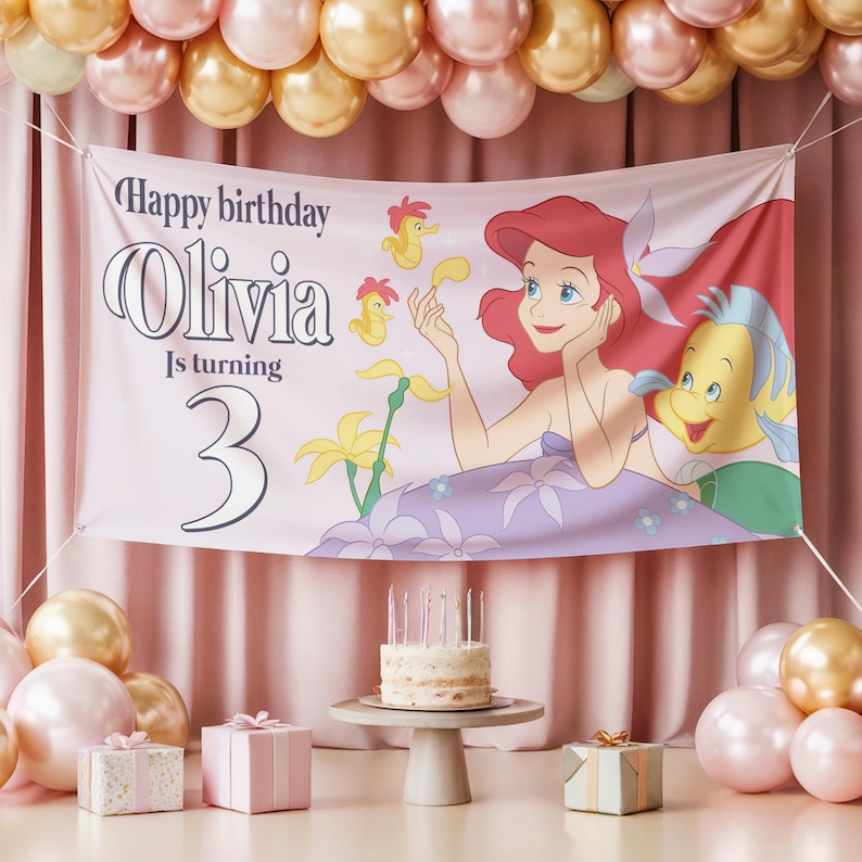 May include: A pink banner with the text "Happy birthday Olivia Is turning 3" and a cartoon illustration of Ariel and Flounder from The Little Mermaid. The banner is decorated with balloons and a birthday cake.