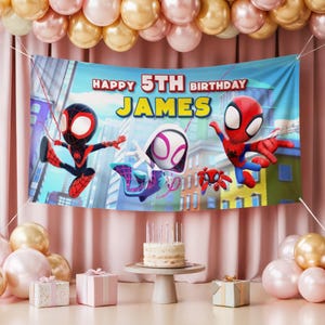 May include: A blue banner with the text "HAPPY 5TH BIRTHDAY JAMES" and cartoon Spider-Man characters. The banner is decorated with balloons and is part of a birthday party setup. A cake and gifts are also visible.
