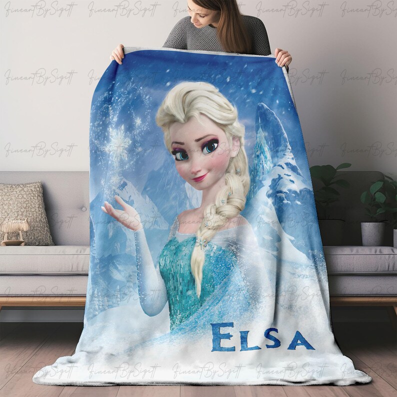 Puede incluir: Una manta suave, azul y blanca con un retrato de Elsa de la pel&iacute;cula Frozen. La manta tiene una imagen detallada de Elsa con un vestido azul, con el nombre "ELSA" impreso en letras grandes en la parte inferior.