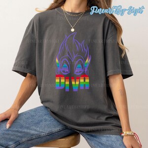Op de afbeelding: Een donkergrijs T-shirt met een paars cartoonfiguur met regenboogogen en het woord "DIVA" in regenboogletters.