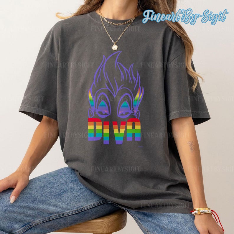 Op de afbeelding: Een donkergrijs T-shirt met een paars cartoonfiguur met regenboogogen en het woord "DIVA" in regenboogletters.