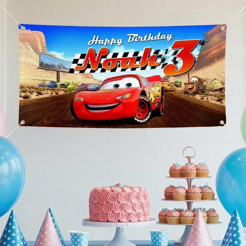 May include: A banner with the text "Happy Birthday Noah 3" featuring the character Lightning McQueen from the movie Cars. The banner is blue with a desert landscape background. Party decorations include a pink cake, cupcakes, and balloons.