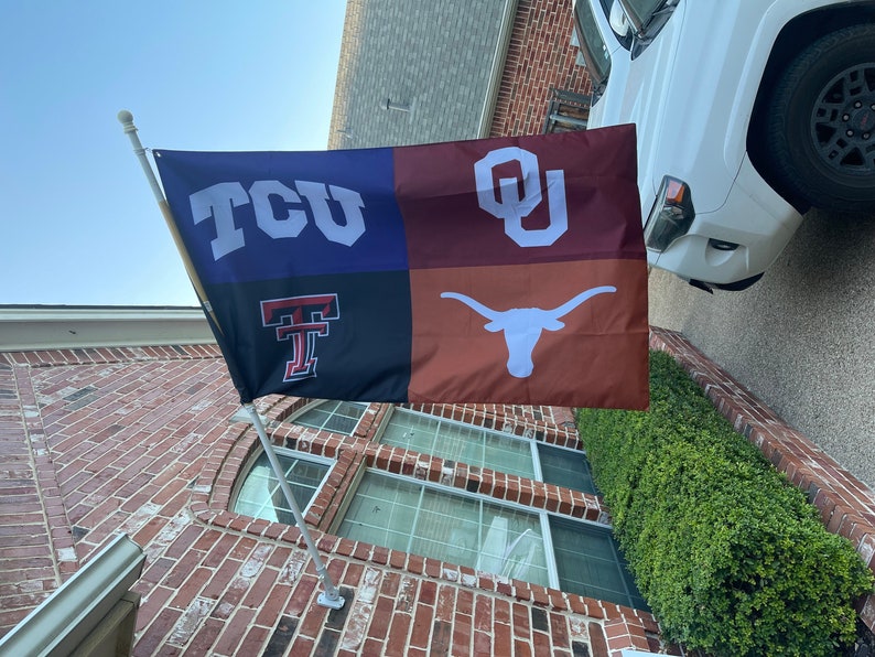 May include: A multi-colored flag with four sections. The top left section is blue with white letters that say "TCU". The top right section is maroon with white letters that say "OU". The bottom left section is black with a red "T" and the bottom right section is orange with a white longhorn steer.