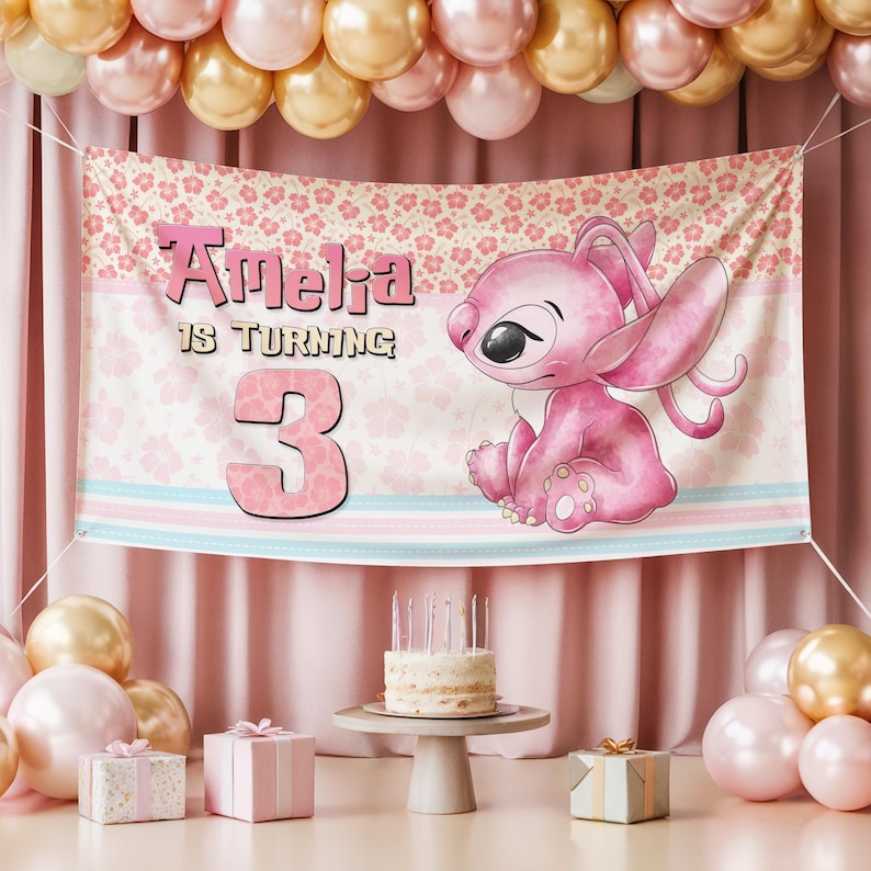 May include: A pink banner with the text "Amelia is turning 3" and a cartoon character. The banner is decorated with floral patterns and pastel stripes. A small cake with candles sits on a pedestal table, surrounded by balloons and gifts.