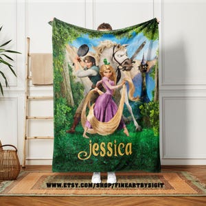 May include: A plush, green blanket featuring a vibrant illustration of a princess with long blonde hair, a prince, and a white horse. The blanket has the name "Jessica" in gold script. The background includes a forest scene and a castle.