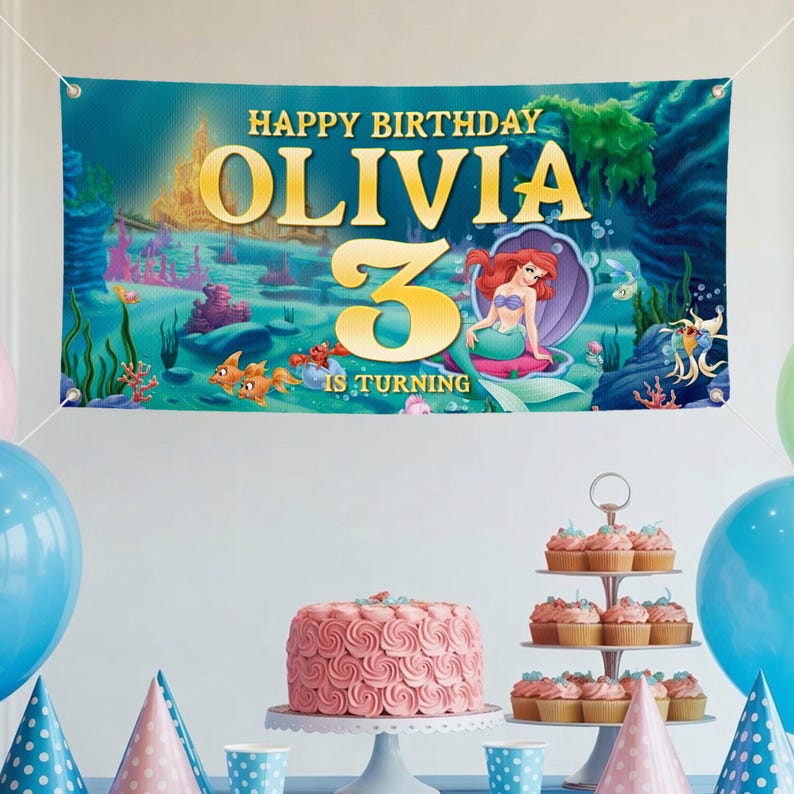 May include: A banner with the text "HAPPY BIRTHDAY OLIVIA 3 IS TURNING" and an illustration of a mermaid in an underwater scene. The banner is above a table with a pink cake, cupcakes, and balloons.
