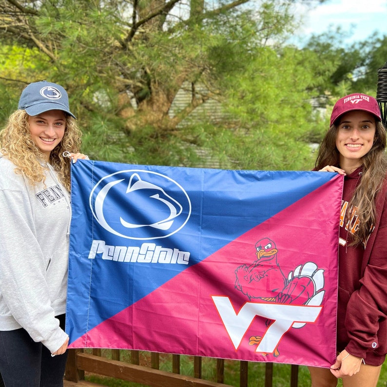 May include: Two people holding a Penn State and Virginia Tech flag. The flag is blue and pink with the Penn State Nittany Lion logo on the blue side and the Virginia Tech Hokie Bird logo on the pink side. The text "Penn State" and "VT" are on the flag.