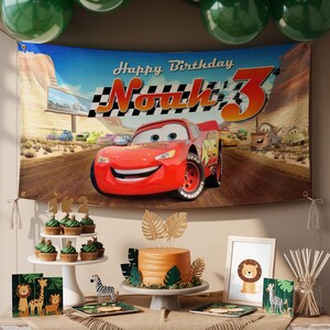May include: A birthday party scene featuring a banner with Lightning McQueen from the movie Cars, with the text "Happy Birthday Noah 3". The table includes cupcakes, a cake, and safari-themed decorations.