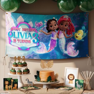 Peut inclure: Sc&egrave;ne de f&ecirc;te d'anniversaire avec une banni&egrave;re repr&eacute;sentant deux sir&egrave;nes et le texte "Happy Birthday Olivia 3 is Turning". La table comprend des cupcakes, un g&acirc;teau et des d&eacute;corations sur le th&egrave;me du safari. Des ballons verts sont visibles en arri&egrave;re-plan.