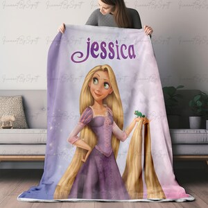 May include: A personalized fleece blanket featuring a cartoon illustration of a princess with long blonde hair, wearing a purple dress. The name "Jessica" is printed in purple script at the top of the blanket. The blanket has a soft, plush appearance.