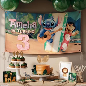 May include: A birthday party setup with a banner featuring Stitch and Lilo, a cake, cupcakes, and decorations. The banner says "Amelia is turning 3." The cake is orange with leaf decorations. Cupcakes have green icing. Additional decorations include framed art and animal-themed place settings.