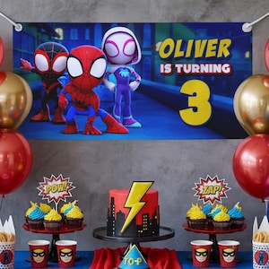 K&ouml;nnte beinhalten: Eine Geburtstagsparty-Szene mit einem Banner mit Spider-Man-Charakteren und dem Text "Oliver wird 3". Der Tisch ist mit einem Kuchen, Cupcakes und Superhelden-Bechern und Dekorationen geschm&uuml;ckt. Rote und goldene Luftballons tragen zur festlichen Atmosph&auml;re bei.