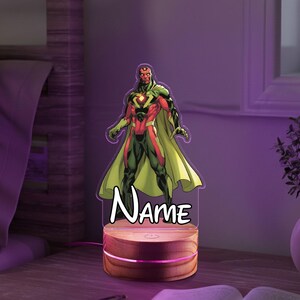 May include: A Vision character night light with a wooden base. The superhero is depicted in a red, green, and black costume with a yellow cape. The word "Name" is written in white script below the character.