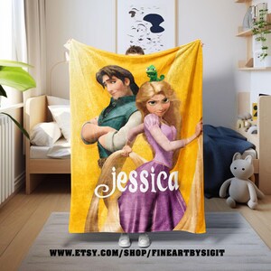 May include: A yellow fleece blanket featuring a cartoon image of Rapunzel and Flynn Rider from the movie Tangled. The blanket has the name "Jessica" in a cursive font. The blanket is a soft, cozy item.