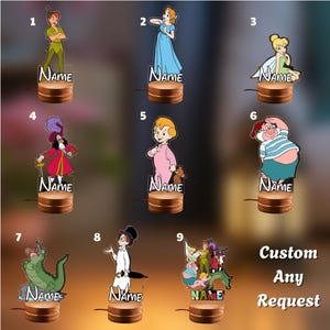 May include: Nine acrylic night lights featuring Peter Pan characters including Peter, Wendy, Tinker Bell, Captain Hook, John, Smee, the crocodile, and Michael. Each figure stands on a round wooden base with the text Name printed on the front.