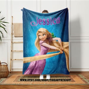 May include: A blue fleece blanket featuring a cartoon illustration of a princess with long blonde hair and a green frog. The name "Jessica" is written in pink script across the top. The blanket has the Etsy shop URL at the bottom.
