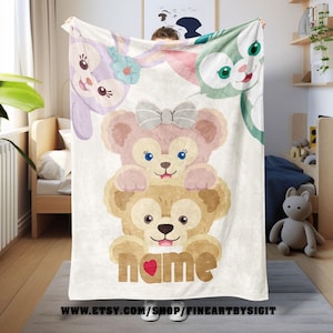 May include: A white blanket featuring cartoon characters, including a bear, bunny, and cat. The bear characters are stacked, with the word "name" and a heart at the bottom. The blanket is held up by a person.