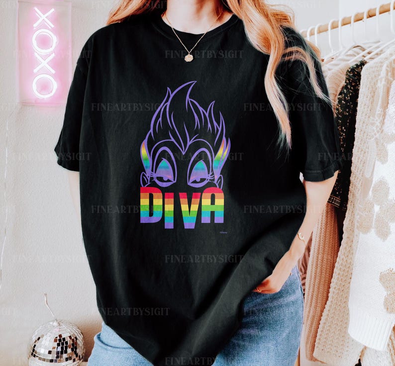 Op de afbeelding: Zwart T-shirt met een paars cartoonfiguur met regenboogtekst die "Diva" zegt.