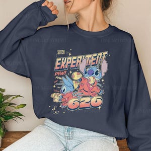 May include: A navy blue sweatshirt with a graphic print of Stitch from Lilo & Stitch. The graphic features Stitch in a red spacesuit with the text "Stitch Experiment 626" and "Pew!" in a retro style.