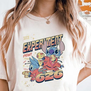 May include: A white t-shirt with a blue and red graphic of Stitch from Lilo & Stitch. The graphic says "Experiment 626" and "Pew!" in a retro font.