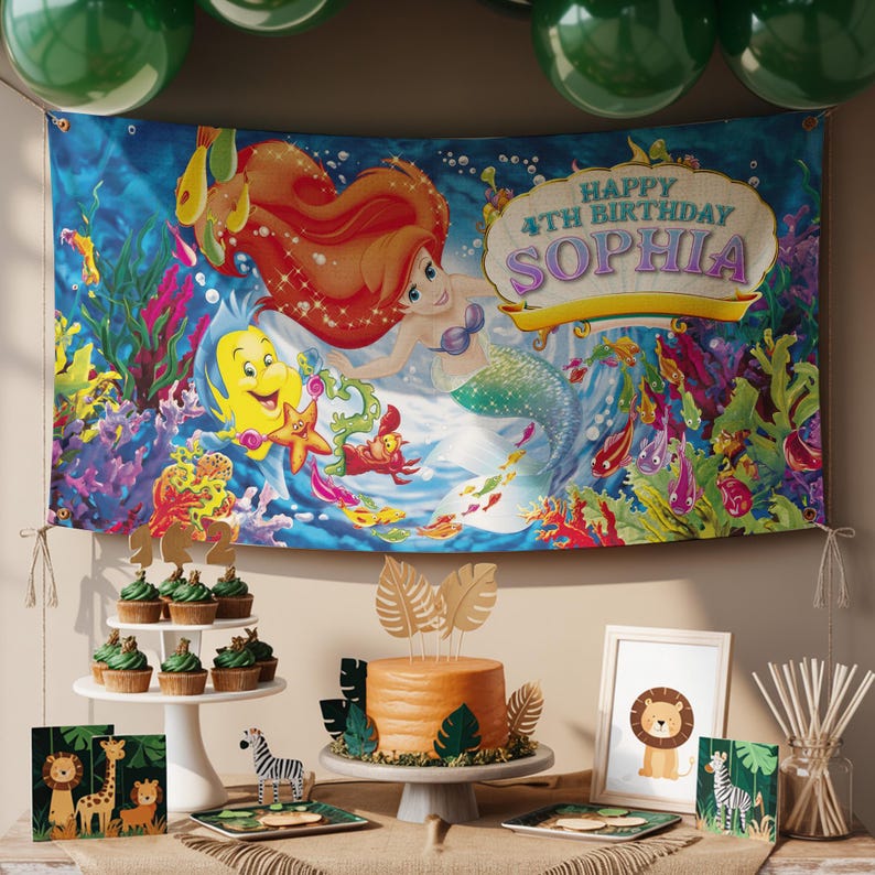 K&ouml;nnte beinhalten: Geburtstagsdekoration mit einem Banner mit einer Meerjungfrau und dem Text "Happy 4th Birthday Sophia". Ein Kuchen, Cupcakes und Tierdekorationen sind arrangiert. Gr&uuml;ne Luftballons sind im Hintergrund zu sehen.
