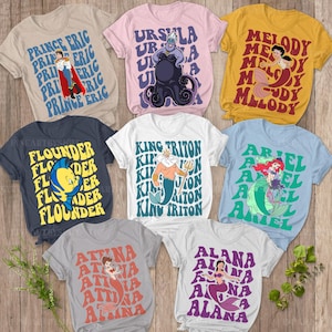 Puede incluir: Una colección de camisetas coloridas con personajes de una popular película animada. Los diseños incluyen al Príncipe Eric, Úrsula, Melody, Flounder, Rey Tritón, Ariel, Attina y Alana. Cada camiseta tiene una ilustración del personaje y su nombre.