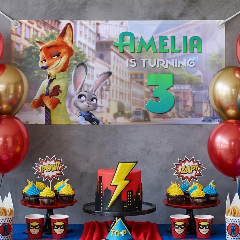 Pu&ograve; includere: Scena di festa di compleanno con uno striscione con la scritta "Amelia compie 3 anni" e personaggi di Zootropolis. Il tavolo &egrave; decorato con cupcakes, una torta con un fulmine e bicchieri e tovaglioli a tema. Palloncini rossi e oro.