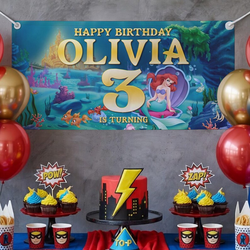 May include: A birthday party scene with a banner that reads "Happy Birthday Olivia 3 is Turning." The banner features an underwater scene with a mermaid. There are red and gold balloons, cupcakes, a cake with a lightning bolt, and superhero-themed cups.