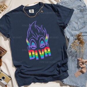 Op de afbeelding: Een marineblauw t-shirt met een regenbooggrafiek van Ursula uit De Kleine Zeemeermin. De grafiek bevat het woord "Diva" in regenboogletters.