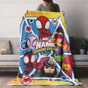 May include: A colorful Marvel "Amazing Friends" blanket featuring Spider-Man, Spider-Gwen, and other characters. The blanket has a blue, red, and yellow design with the Marvel logo and character names. The blanket is made of soft material.