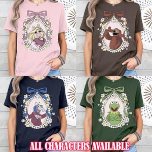 May include: Four different t-shirts featuring Muppet characters in a vintage-inspired frame. The shirts are pink, brown, navy blue, and green. Each shirt features a different Muppet character: Miss Piggy, Animal, Gonzo, and Kermit the Frog. The text "ALL CHARACTERS AVAILABLE" is at the bottom of the image.