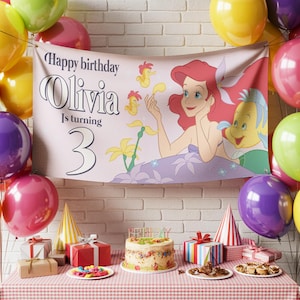 May include: A birthday party scene with a banner featuring Ariel from The Little Mermaid, balloons, gifts, and a cake. The banner reads "Happy birthday Olivia is turning 3." The table is set with a red and white checkered tablecloth.