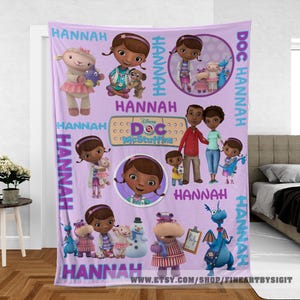May include: A lavender fleece blanket featuring cartoon characters from the Disney show Doc McStuffins. The blanket has images of the main character, her family, and various toy friends. The name "Hannah" is printed throughout the design.