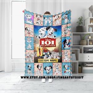 May include: A soft, blue and beige fleece blanket with a collage of images from the Disney movie 101 Dalmatians. The blanket features a large image of Cruella De Vil and the Dalmatian puppies, along with smaller images of the Dalmatian puppies in various poses. The blanket also includes the text "Disney 101 Dalmatians" and "CUSTOM NAME".