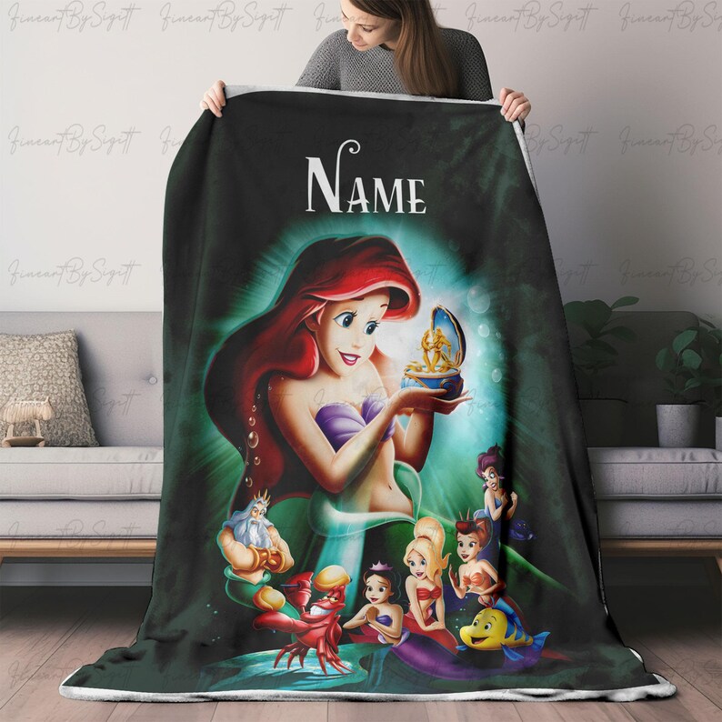 May include: A plush, personalized blanket featuring Ariel from The Little Mermaid. The design showcases Ariel with red hair, a purple top, and a green tail, surrounded by other characters. The word "Name" is displayed at the top.