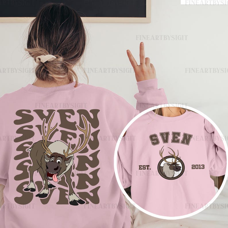 May include: Pink sweatshirt featuring a cartoon reindeer with the name "SVEN" in brown lettering. The design includes a circular graphic with the reindeer and the text "EST. 2013". The sweatshirt is a light pink color.