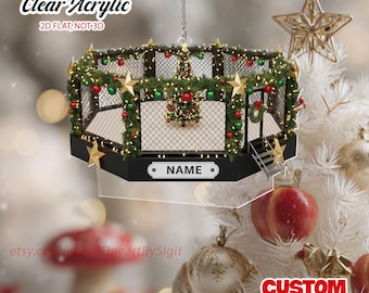 May include: Clear acrylic Christmas ornament shaped like a mixed martial arts cage, decorated with garland, lights, and ornaments. The ornament has a black base and features the text "NAME". The text "Clear Acrylic 2D FLAT; NOT 3D" is also visible.