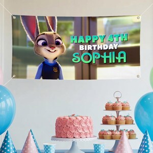 May include: A birthday banner featuring Judy Hopps from Zootropolis, with the text "HAPPY 4TH BIRTHDAY SOPHIA." A pink cake and cupcakes are on display. The banner is white with eyelets in each corner.
