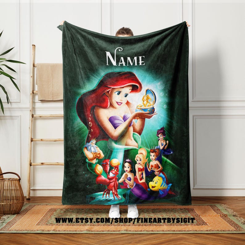 May include: A dark green fleece blanket featuring a colorful illustration of Ariel from The Little Mermaid. The image includes Ariel holding a treasure, with other characters from the movie. The word "Name" is at the top.