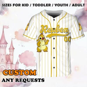Puede incluir: Jersey de b&eacute;isbol blanco con rayas amarillas y un personaje de dibujos animados. El jersey tiene el nombre "Reuben" y el n&uacute;mero "00" en la espalda. El texto "CUSTOM ANY REQUESTS" est&aacute; en la parte inferior de la imagen.