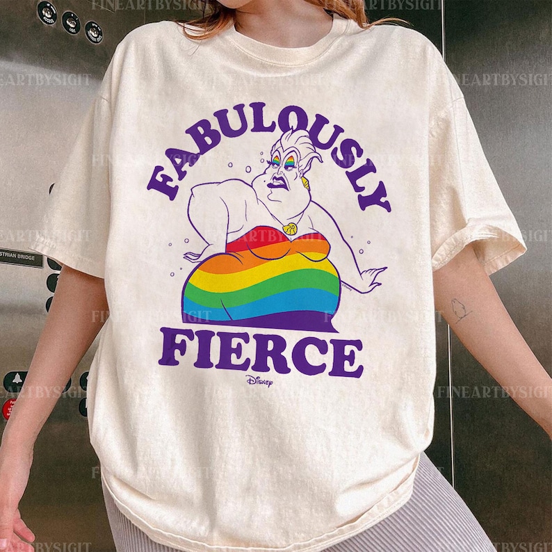 Peut inclure: T-shirt cr&egrave;me avec une illustration de dessin anim&eacute; d'Ursula de La Petite Sir&egrave;ne de Disney. Le personnage est repr&eacute;sent&eacute; avec une jupe aux couleurs de l'arc-en-ciel et les mots "FABULOUSLY FIERCE" en violet. Le t-shirt a des manches courtes.