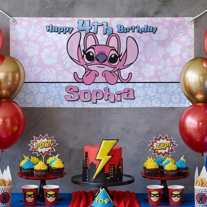 Op de afbeelding: Een verjaardagsfeestje met een banner met de tekst "Happy 4th Birthday Sophia" met een roze stripfiguur. De tafel bevat een taart met een bliksemontwerp, cupcakes en bekers en decoraties met superheldenthema. Rode en gouden ballonnen maken de feestelijke setting compleet.