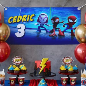 May include: A birthday party scene with a banner that says "CEDRIC 3" and features cartoon Spider-Man characters. The table is decorated with a cake, cupcakes, and superhero-themed cups and decorations. Red and gold balloons are also present.