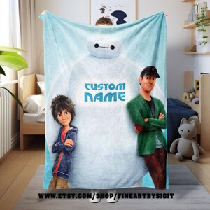 May include: A light blue blanket featuring characters from the animated movie Big Hero 6. The blanket has a large image of Baymax with the text "CUSTOM NAME" in blue. Hiro Hamada and Tadashi Hamada are also featured on the blanket.