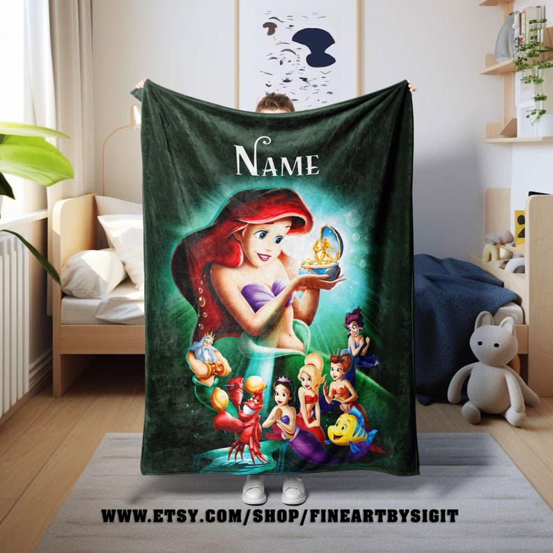 May include: A dark green fleece blanket featuring a colorful illustration of Ariel from The Little Mermaid. The image includes Ariel, Flounder, Sebastian, and other characters. The blanket has the word "Name" at the top and the Etsy shop URL at the bottom.